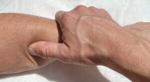 Mains en auto-massage du bras, pression sur zone douloureuse